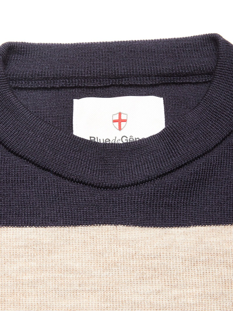 Close-up of the Blue de Gênes Toyama Stripe Knit L/S in dark navy, featuring a crewneck with a white label inside the collar showing a red shield emblem, Blue de Gênes text, and a stylish beige panel below the collar.
