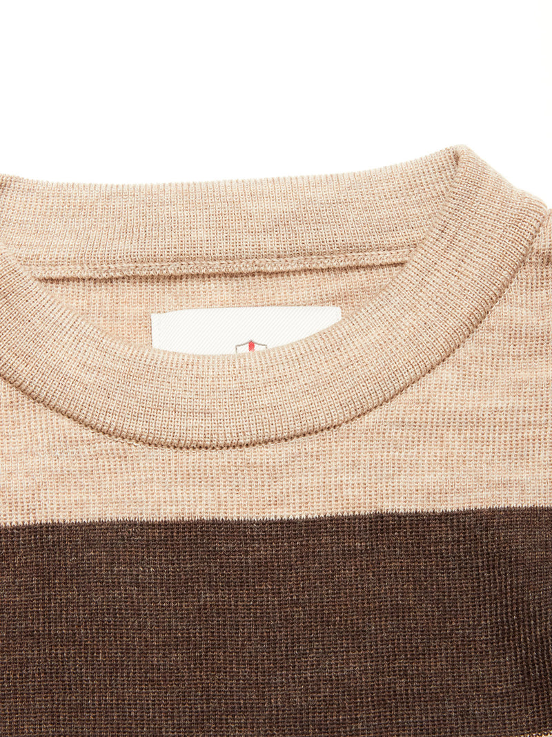 Close-up of the Blue de Gênes Toyama Stripe Knit L/S - Oat, showing a ribbed beige crewneck collar, horizontal brown stripe underneath, and a partially visible white tag with red detail inside the collar.