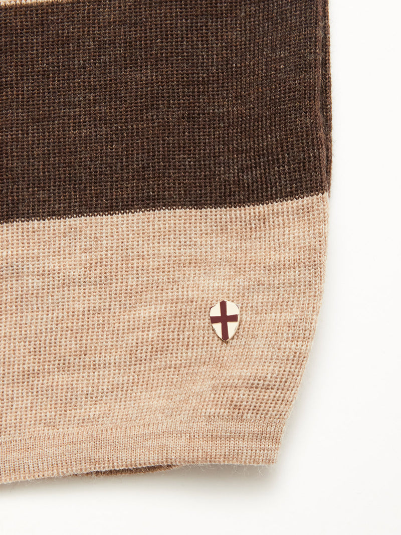 The Toyama Stripe Knit L/S - Oat by Blue de Gênes features wide brown and beige stripes and a small shield-shaped emblem with a brown cross near the hem.