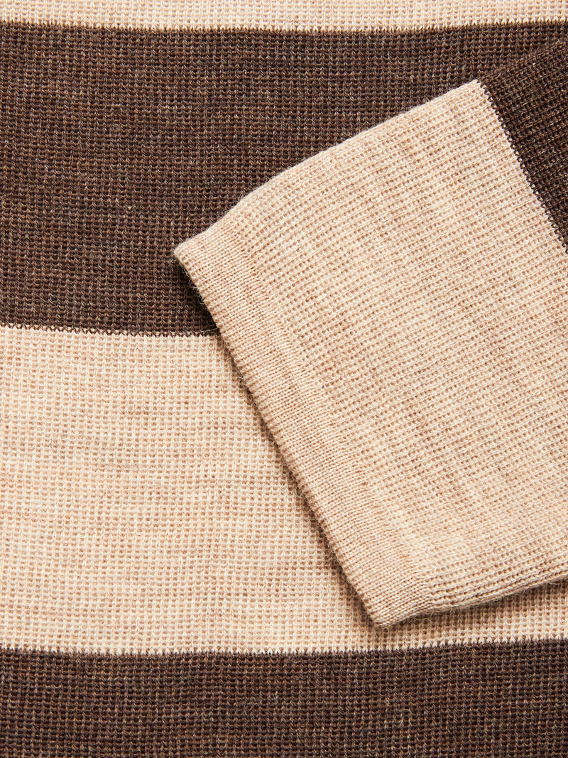 A close-up of the Blue de Gênes Toyama Stripe Knit L/S - Oat, featuring wide brown and beige horizontal stripes with a folded section arranged diagonally across the soft knit fabric.