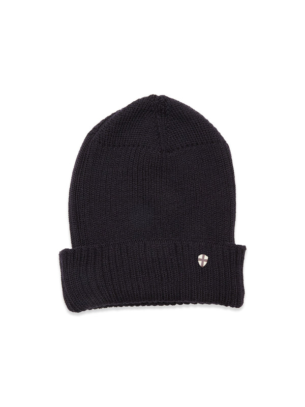 The Boshi Beanie in dark navy by Blue de Gênes is rib-knitted in Denmark with a folded brim and features a small round metal shield emblem on the front.