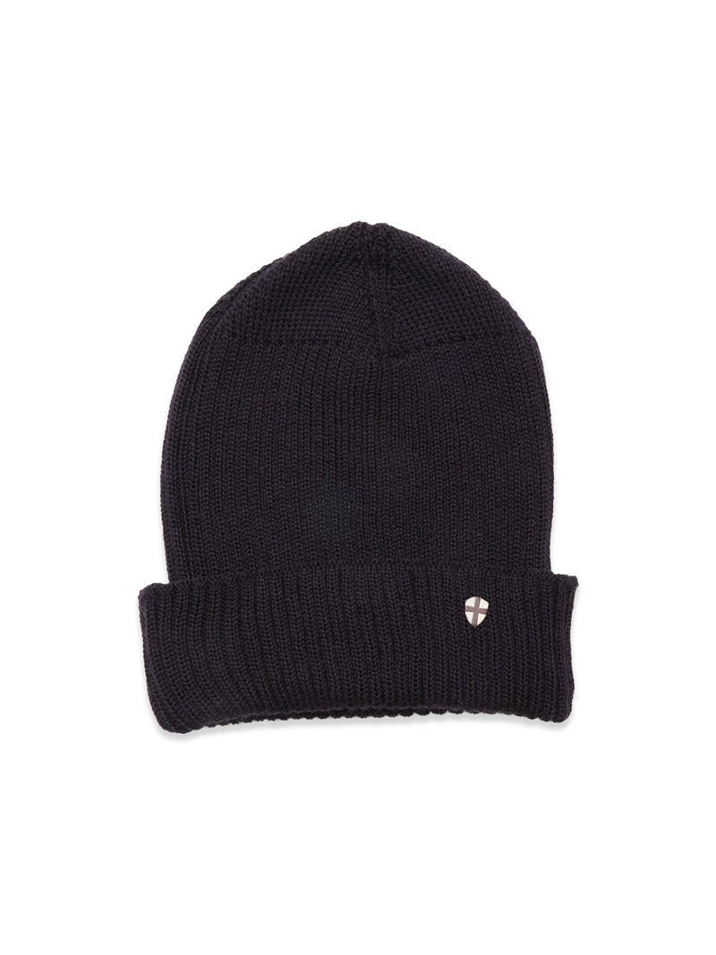 The Boshi Beanie in dark navy by Blue de Gênes is rib-knitted in Denmark with a folded brim and features a small round metal shield emblem on the front.