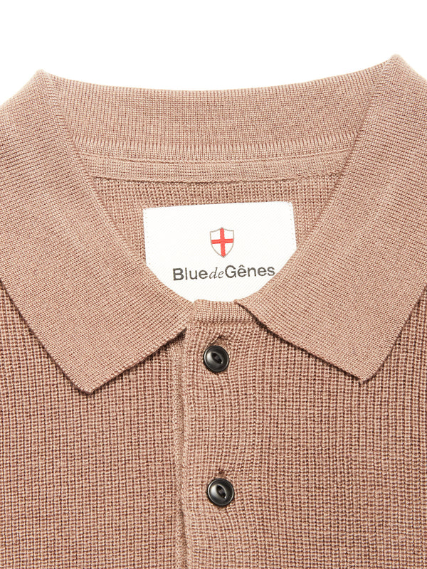 Close-up of the textured, light brown Porto Polo Knit - Fungi shirt by Blue de Gênes, featuring two black buttons and a collar label with the brand name and red cross emblem—a wool polo that exudes casual elegance.