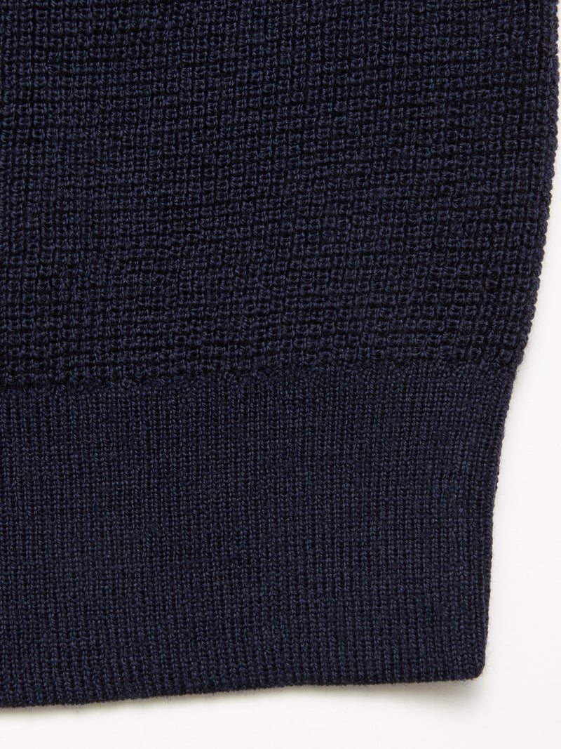 Close-up of the Blue de Gênes Porto Polo Knit in navy, featuring a tighter ribbed hem and fine wool knit texture, showcasing the casual elegance of this polo shirt against a light background.