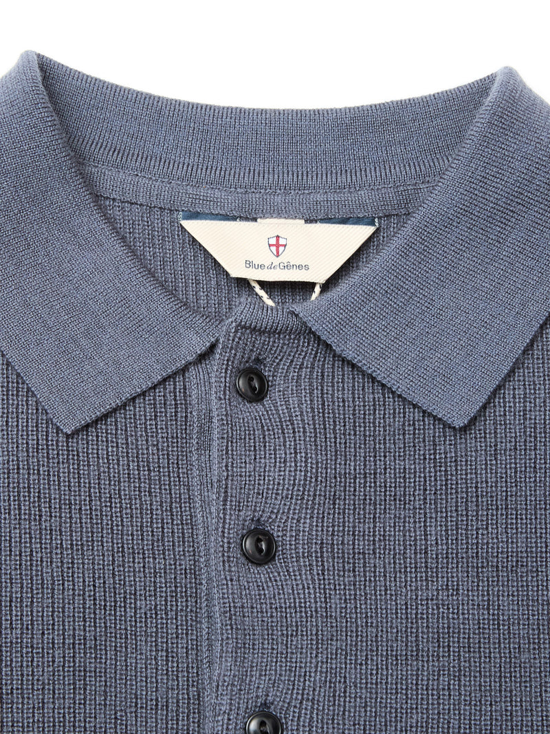 Close-up of the Blue de Gênes Porto Polo Knit - Dark Slate, featuring a textured blue fabric, collar, and black buttons. Inside the collar is a small white tag with the brand name and red-blue shield logo—true luxury knitwear craftsmanship.