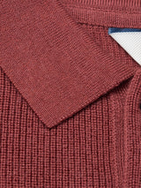 Close-up of the Blue de Gênes Porto Polo Knit in Henna, featuring textured ribbed maroon knitwear, a collar, and a partial white label with a blue edge visible in the top right corner.