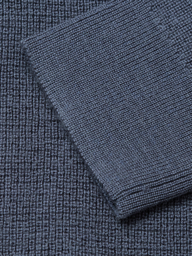 Close-up of a ribbed, dark slate knit fabric from the Porto Polo Knit by Blue de Gênes, with a folded section diagonally across the surface to showcase its luxurious texture and pattern.