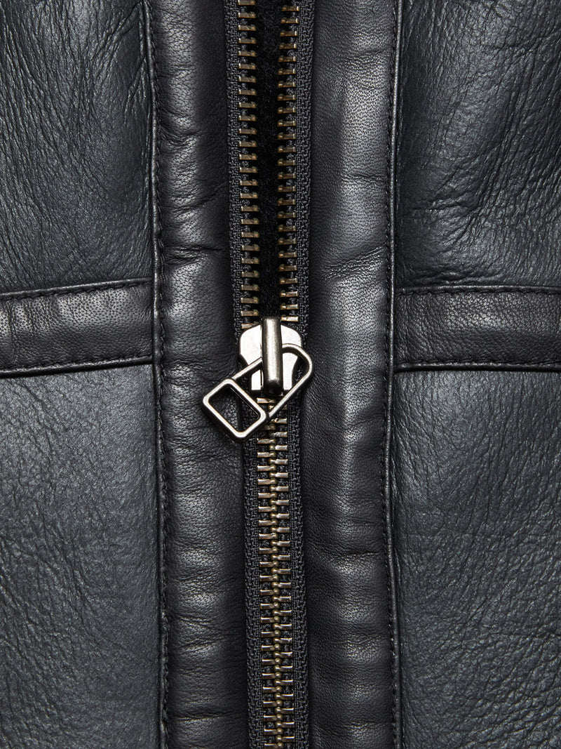 Close-up of the Saga Shearling Gilet - Scarab by Blue de Gênes, showing textured black leather, detailed stitching, and a silver zipper, expertly crafted from premium German Merino sheepskin.