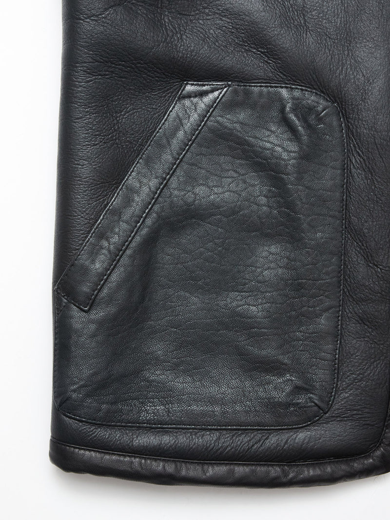 Close-up of the Saga Shearling Gilet - Scarab by Blue de Gênes, highlighting the angled pocket and intricate stitching on smooth black German Merino sheepskin, with its detailed texture and subtle shine.