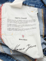 The white fabric label inside Marco Used Jeans - Used by Blue de Gênes features brand logos, 100% cotton denim text, black script at the bottom, visible red stitching, and denim edges.