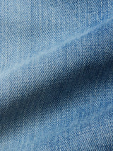 Close-up of light blue 100% cotton denim fabric from Blue de Gênes Marco Used Jeans - Used, highlighting detailed texture, diagonal weave pattern, and subtle fabric fold shadows.