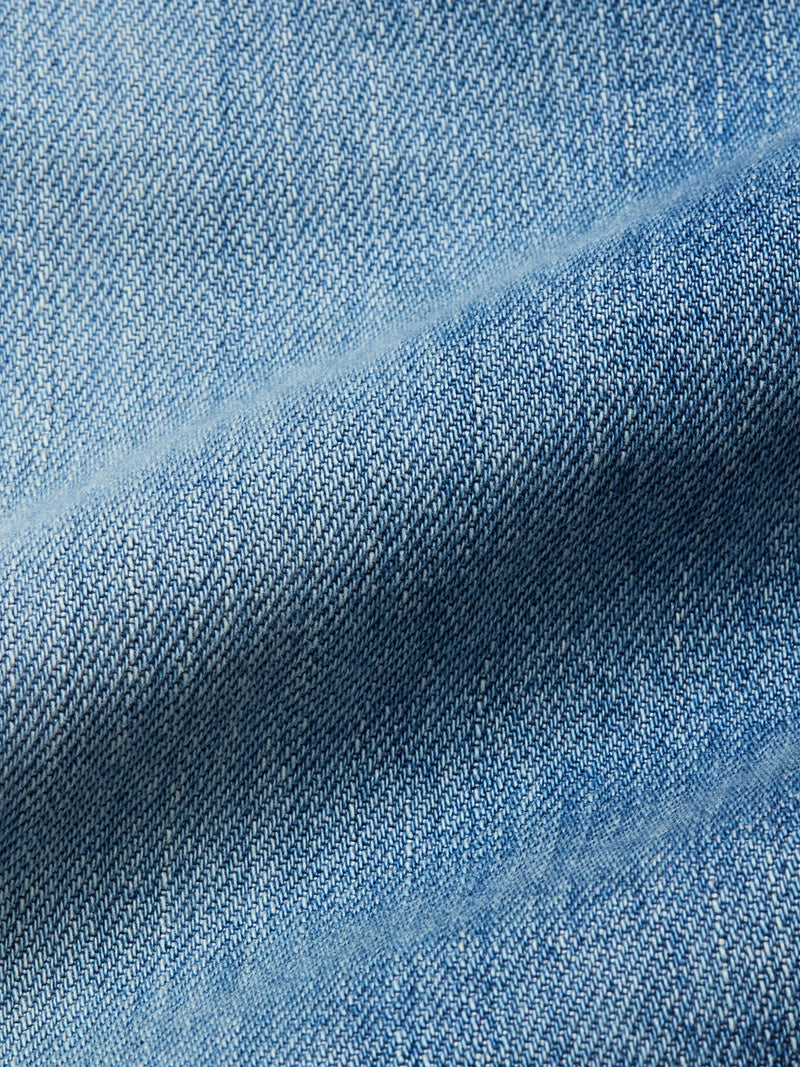Close-up of light blue 100% cotton denim fabric from Blue de Gênes Marco Used Jeans - Used, highlighting detailed texture, diagonal weave pattern, and subtle fabric fold shadows.