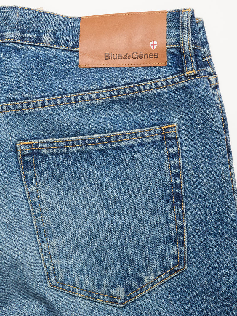 Close-up of the back pocket and waistband of Marco Used Jeans - Used by Blue de Gênes, made in Greece from blue 100% cotton denim. Features a brown leather brand patch with shield logo, visible stitching, and a faded, worn finish.