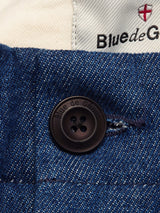 Close-up of blue denim fabric in a heavy cotton blend with a black Blue de Gênes button. The Shogun Fano Pant - Denim Blue features white waistband lining, Blue de Gênes branding, and a small red emblem.