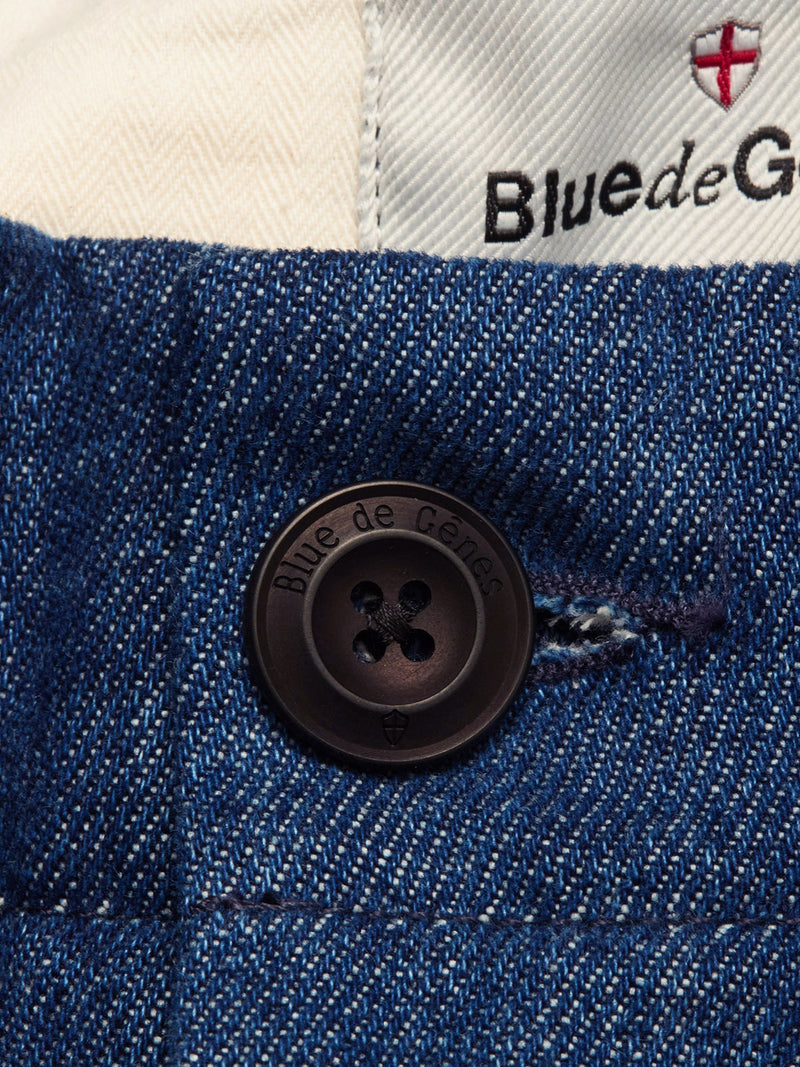 Close-up of blue denim fabric in a heavy cotton blend with a black Blue de Gênes button. The Shogun Fano Pant - Denim Blue features white waistband lining, Blue de Gênes branding, and a small red emblem.