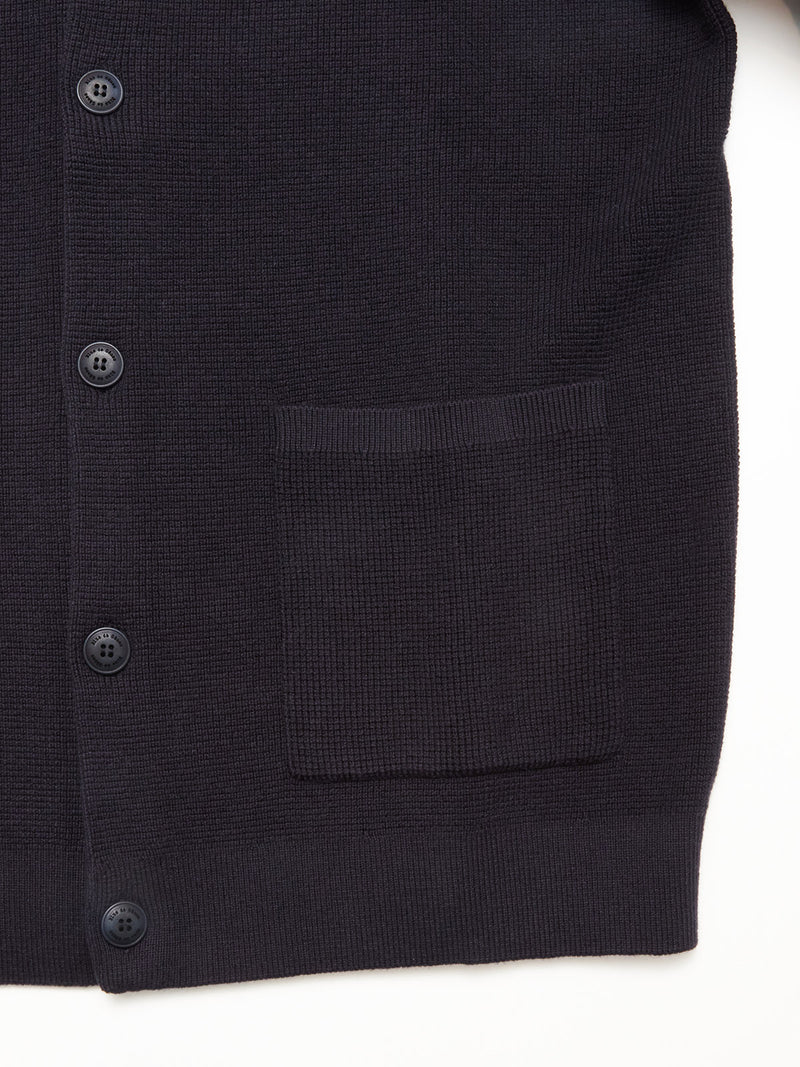 Close-up of the Blue de Gênes Gifu Knit Cardigan in navy, showcasing black buttons, a single front pocket, and a visible knit texture with ribbed hem. Wool blend. Set against a white background.