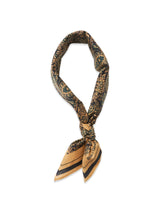 The Siruku Scarf - Mixed Colours by Blue de Gênes is a patterned silk scarf in gold and black with an ornate flower print, tied in a loose knot, and the text B-LA-GE visible on one pointed end.