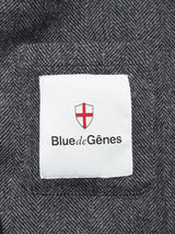 A white fabric label on the black-patterned Fukui Blazer by Blue de Gênes features a red cross on a shield with the brand name displayed below.
