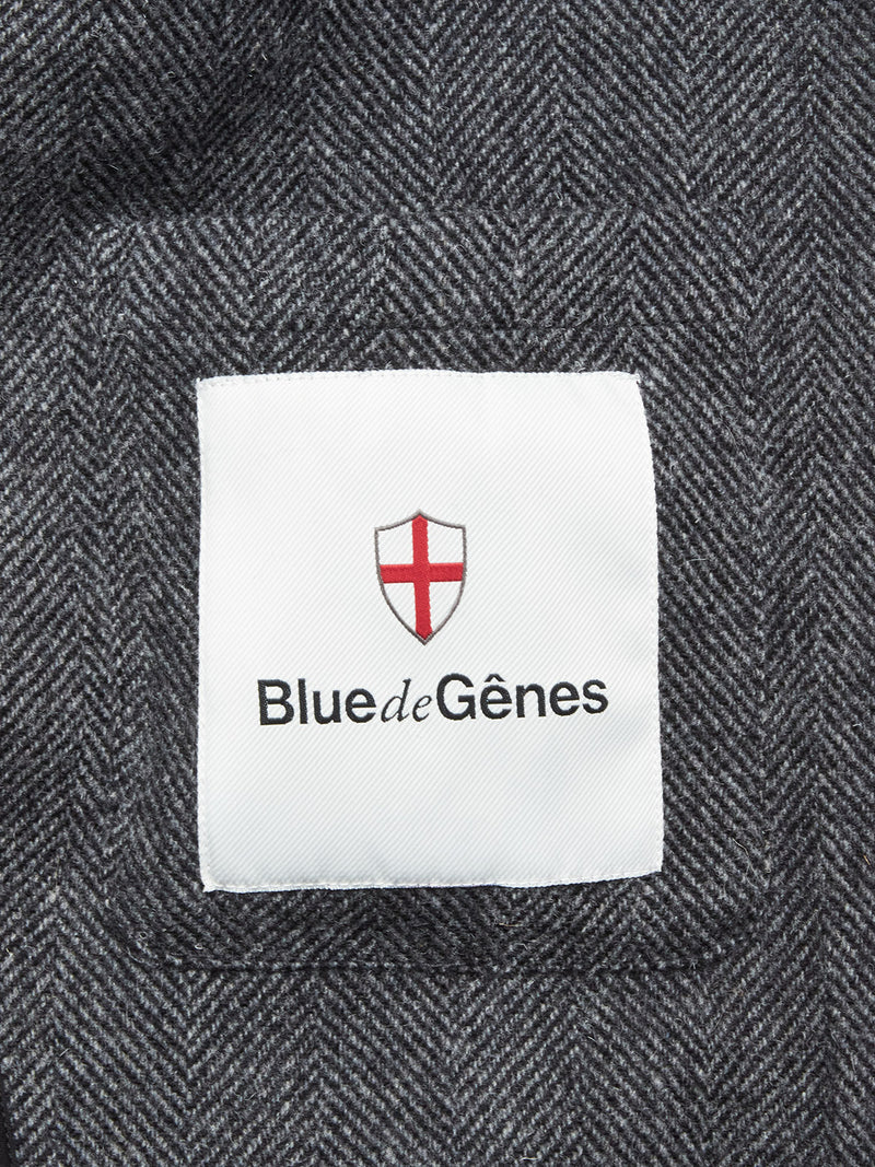 A white fabric label on the black-patterned Fukui Blazer by Blue de Gênes features a red cross on a shield with the brand name displayed below.