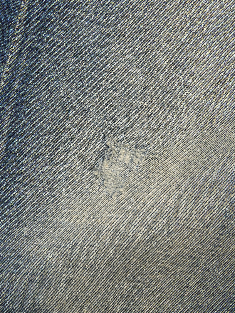 A close-up of Blue de Gênes Vinci Dark Vintage Jeans in mid blue denim highlights a discreet, faded patch repaired with lighter thread, seamlessly blending into the fabric.