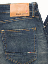 Close-up of the back of Vinci Dark Vintage Jeans in mid blue denim by Blue de Gênes, showing orange stitching, a brown leather Blue de Gênes patch, and an embroidered striped detail on the five-pocket jean’s back pocket.
