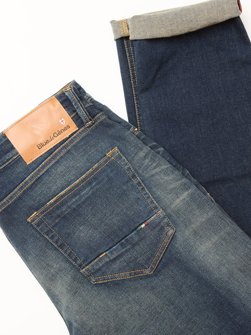 Two pairs of Blue de Gênes jeans are shown on a white background: one is the Vinci Dark Vintage Jeans in mid blue denim with a turned-up cuff, while the other features faded denim, visible stitching, and a brown leather brand label.