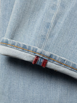A close-up of Blue de Gênes BGvinci Trueblue Jeans in mid blue denim highlights the cuffed hem with orange stitching and a red and blue striped tab on the seam, made from comfort stretch fabric.