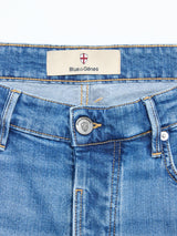 A close-up of BGvinci Hera Used Jeans by Blue de Gênes in blue-black denim, featuring a waistband, metal button with shield logo, belt loops, front pockets, and a Blue de Gênes label with a cross emblem.