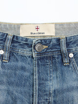 Close-up of the waistband and top front of BGgiacomo Tim Jeans - Antique wash by Blue de Gênes, featuring a button with a crest, belt loops, and a label displaying “Blue de Gênes” beneath a red and white cross emblem.