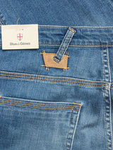 Close-up of BGrepi Misto Jeans - Med Used by Blue de Gênes, featuring blue denim with yellow stitching, a brown leather patch above the back pocket, and a branded tag near the waistband.