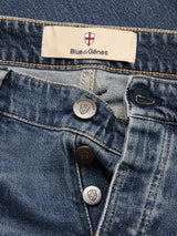 Close-up of BGvinci Striker Jeans - Dark Distress by Blue de Gênes, featuring an open fly with three shield-engraved metallic buttons and a comfort stretch denim. The label above the waistband displays the Blue de Gênes name with a red and white shield logo.