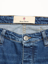Close-up of BGrepi Kanto Jeans - Used by Blue de Gênes shows the blue slim-fit waistband, a metal button engraved with a shield logo, and an inside tag labeled Blue de Gênes with a red and white shield emblem.