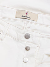 Close-up of BGvinci Bianco Jeans - White by Blue de Gênes, highlighting the waistband label with brand and red-and-white shield logo, plus three metallic buttons engraved with the same shield emblem.