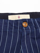 Close-up of the waistband of Blue de Gênes BGpalco Toll Pants - Navy Stripe, featuring white vertical stripes, a brown button, and a beige inner tag with a red and white shield logo.