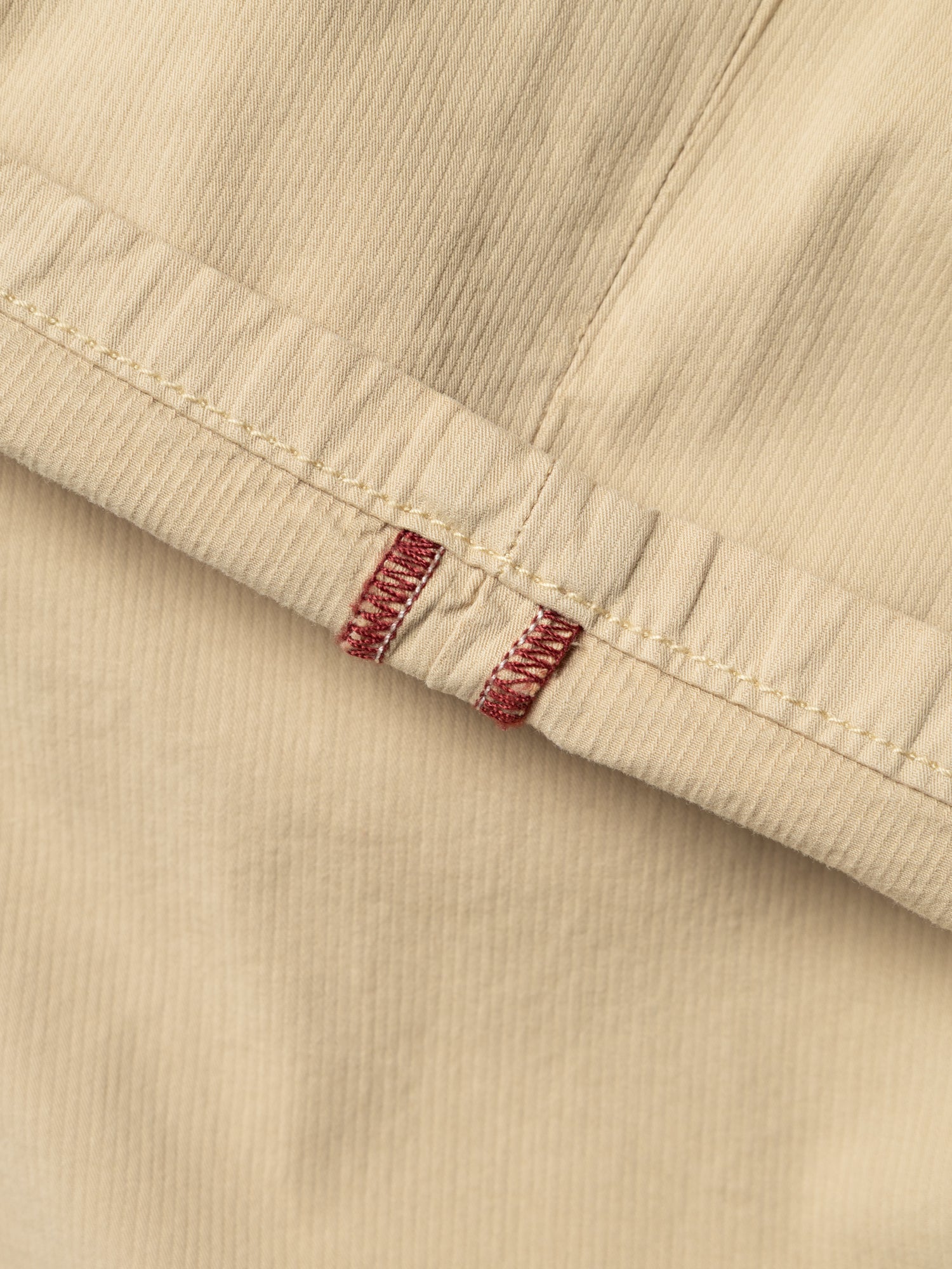 Close-up of pale khaki corduroy fabric from the Blue de Gênes BGmenzo Vecchio Chino, featuring a visible seam and two red stitched bar tacks that highlight its vintage-inspired design.