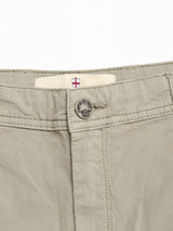 Close-up of the waistband on Blue de Gênes BGmenzo Vecchio Chino in Shadow Green, featuring comfort stretch, metallic button, visible stitching, and a small tag with a red and white shield above the buttonhole for a vintage touch.