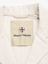 A close-up of the BGbaio Twill Blazer - Chalk by Blue de Gênes, showing its beige cotton twill collar and an inner label with a red and white shield emblem and the brand's name.