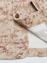 A close-up of the BGkendrick Print Jacket - Multi Pattern by Blue de Gênes, showing its beige cotton twill with brown speckles, a brown button, neatly folded cuff, and partially visible inner white lining.