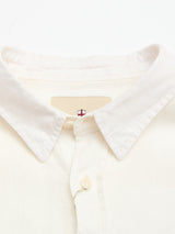 Close-up of the Blue de Gênes BGenric Hope L/S Shirt in Chalk. This off-white linen shirt features a cut-away collar, top button, and an inside tag with a red and blue cross logo. Neatly folded, it embodies breathable summer style.