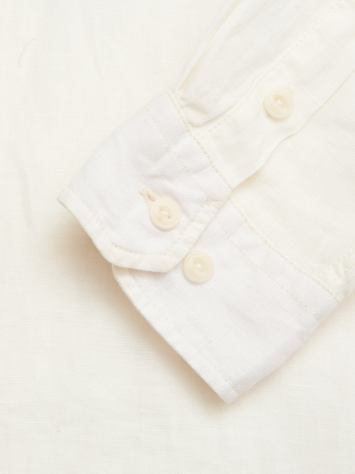 A close-up of the cuff of the Blue de Gênes BGenric Hope L/S Shirt in Chalk, showing two cream-colored buttons, laid flat on a matching white background.