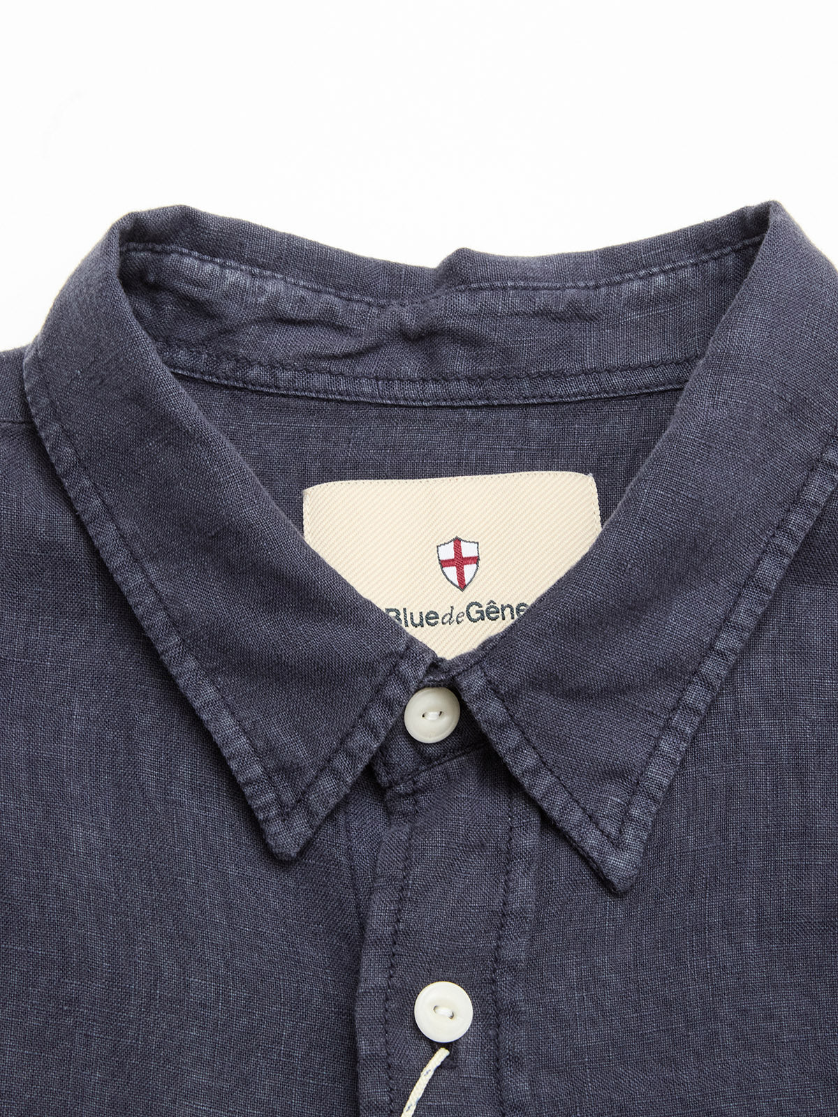 Close-up of the collar and upper buttons of the BGenric Hope S/S Shirt in dark navy linen by Blue de Gênes, featuring a breathable summer design and a white collar label with a red and white shield logo.