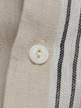 Close-up of a white button sewn onto pale khaki fabric with two black stripes, showcasing the refined details of the Blue de Gênes BGcody Fling Shirt.