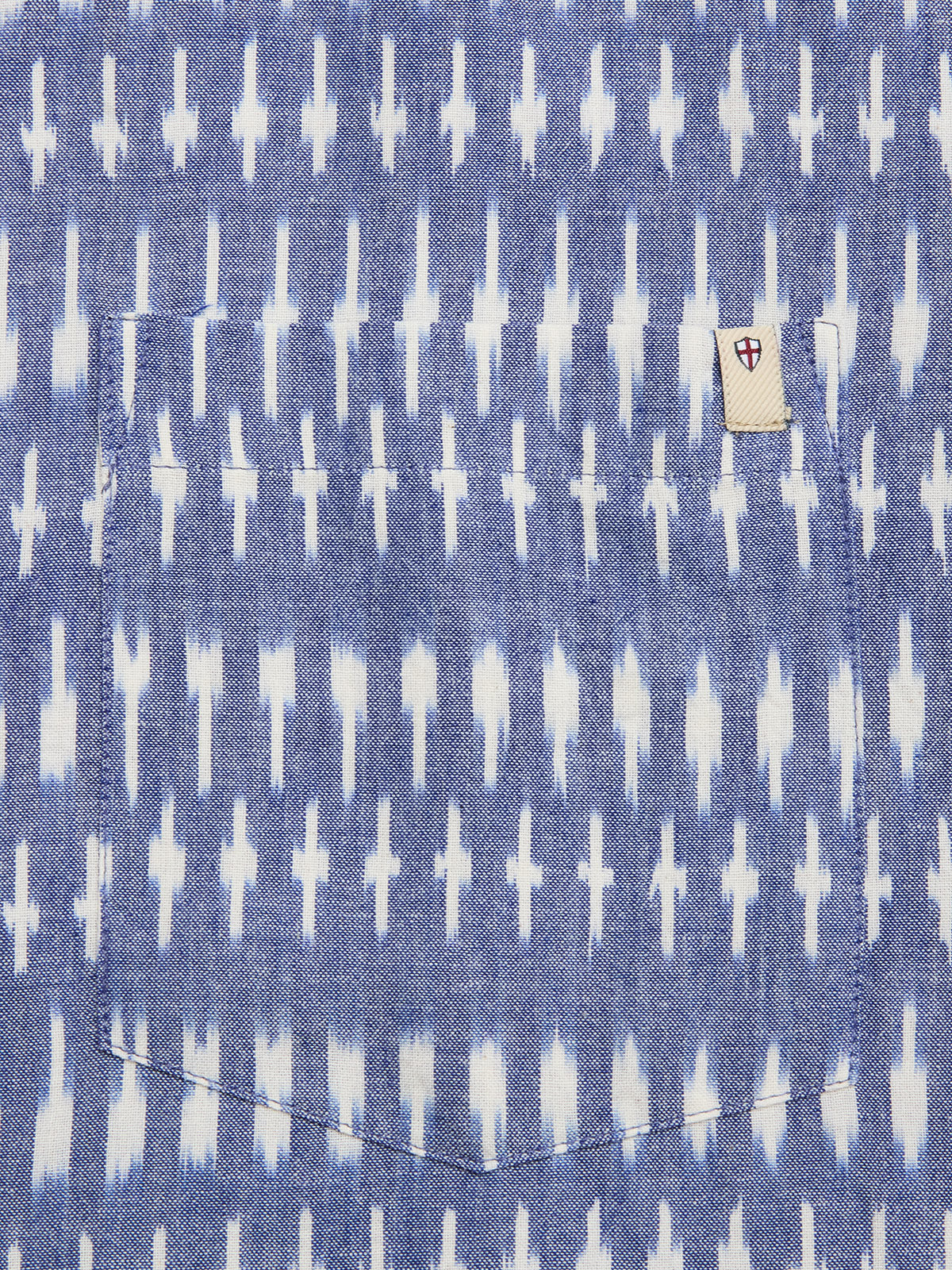 The BGforma Onda S/S Shirt - Blue Pattern by Blue de Gênes features a blue fabric pocket with a white geometric, ikat-style pattern and a small white tag above the pocket with a red and blue shield design.