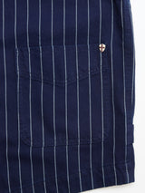 Close-up of the BGlumen Toll Gilet by Blue de Gênes in navy stripe cotton, showing white pinstripes, a sewn-on pocket, and a small shield-shaped emblem—details inspired by traditional workwear.