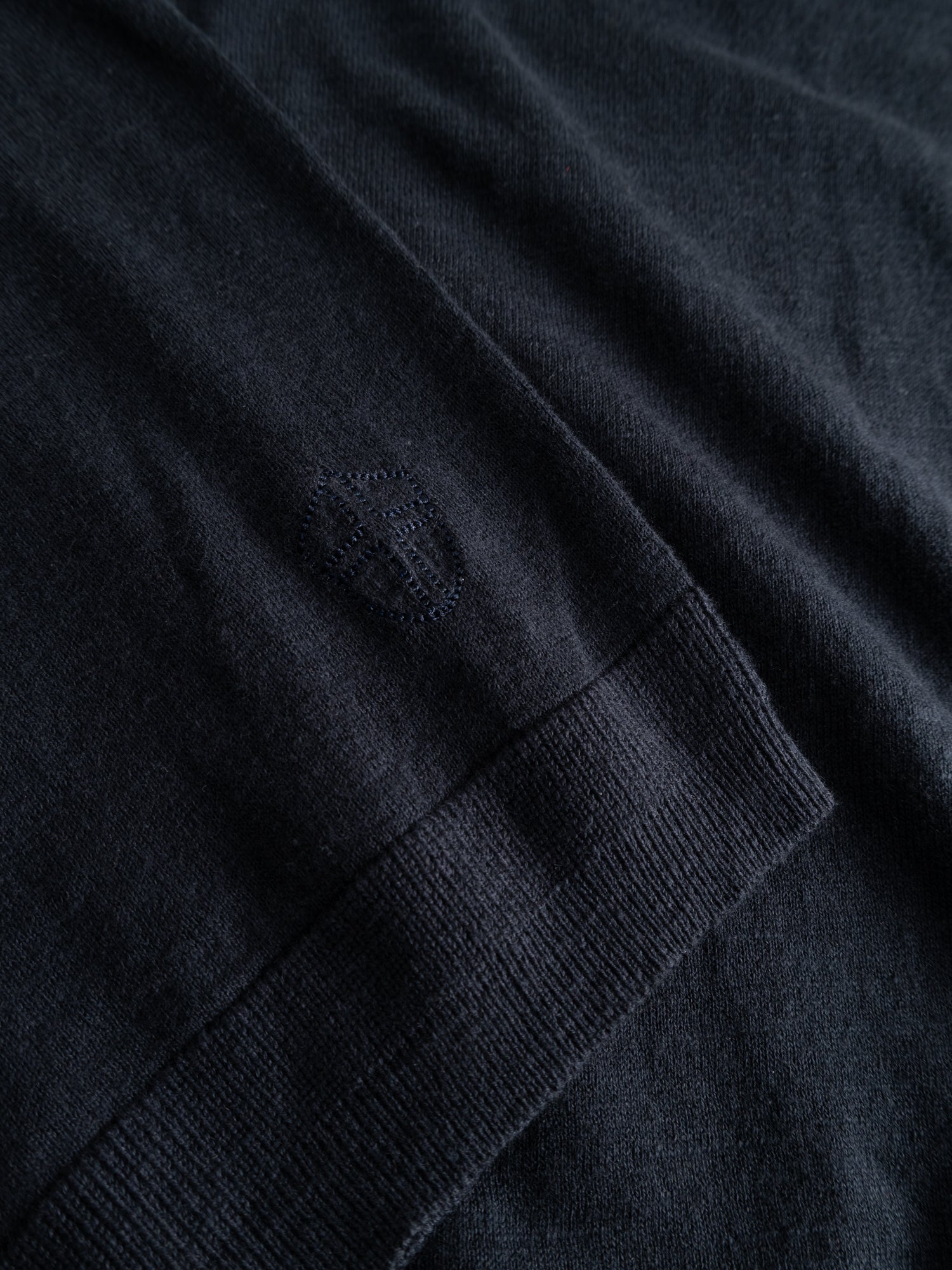 Close-up of the BGmonty Knit in Dark Navy by Blue de Gênes, featuring cotton-linen blend knit, subtle embroidered logo, and ribbed roll-rib hem detailing.
