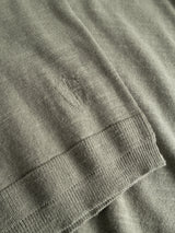 Close-up of the Blue de Gênes BGmonty Knit in Shadow Green, a crewneck featuring a ribbed hem and a small, neatly sewn oval patch repair on its cotton/linen blend fabric.