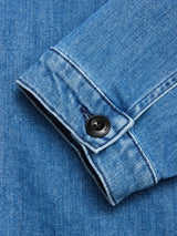 Close-up of the BGpontus Denim Overshirt - Used by Blue de Gênes, showing its blue cotton blend sleeve with a black button and detailed stitching, laid flat on matching denim.