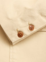 Close-up of the BGnorly Rodas Blazer by Blue de Gênes in pale khaki, showing beige cotton-hemp blend fabric and two brown buttons with black text, suggesting a relaxed fit design.