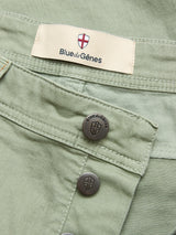 Close-up of BGpaulo Pavia Pant in Shadow Green by Blue de Gênes, in stretch cotton, with metal shield-embossed buttons and a Blue de Gênes fabric label featuring a red and white shield.