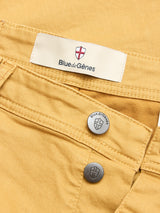 Close-up of BGpaulo Pavia Pant - Sunflower by Blue de Gênes: vintage military-inspired yellow chinos with metal buttons, shield emblem, engraved brand name, and visible stitching on cotton stretch fabric.